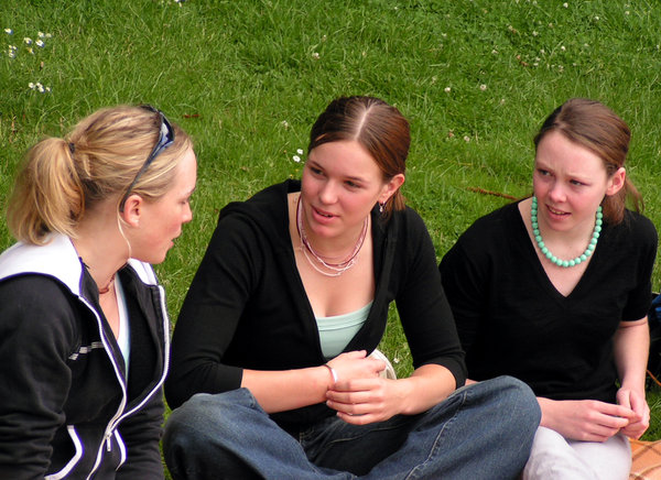 Teen talk: 3 teenage girls.  Must be a fascinating conversation judging by their expressions.  Summer picnic on the grass.  Isn't it funny to see that even when allowed to wear what they want, teens still seem to wear 