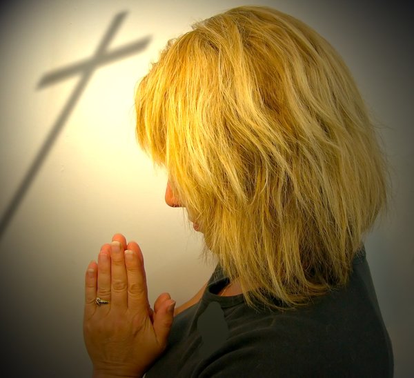 Easter Prayer: A woman praying, with the shadow of a cross in the background. Special light.