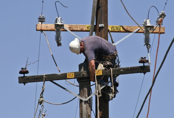 Man Replacing Power Pole: A crane drops a new power pole into a hole next to the one they are replacing. A worker transfers the hardware and hooks up the wires to the new pole.