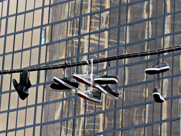 city shoes suspension: several pairs of shoes and sneakers hanging on central city street overhead powerlines