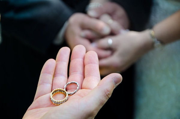 Wedding Rings: Wedding rings in priests hands with marriage couple hands in background