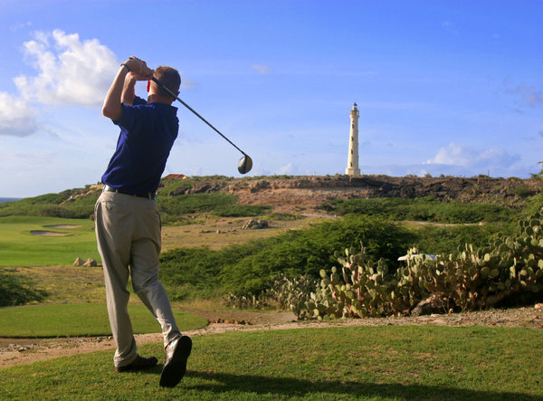 Aruba Golf: Golfer tees off on an Aruba Golf Course. Lighthouse in background