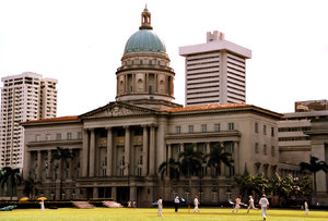 cricket before the courts: a game of cricket being played at the cricket grounds in  front of the Singapore old high court building