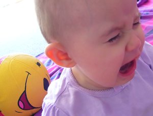 Baby Crying: A baby crying, contrasted with a happy face on a toy in the background. I wish the child was clearer, but I hope it's useful.